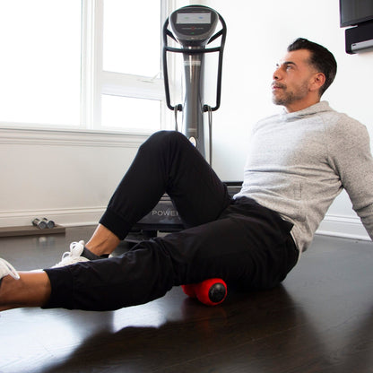 Man using Power Plate vibrating roller on upper hamstrings for muscle recovery at home