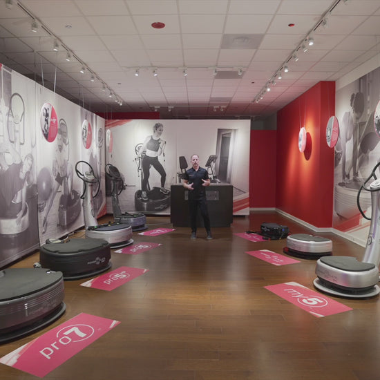 Showroom display featuring multiple Power Plate vibration plate models, including Pro7HC, Pro7, Pro5, My7, My5 and MOVE, arranged on a wooden floor with branded wall graphics
