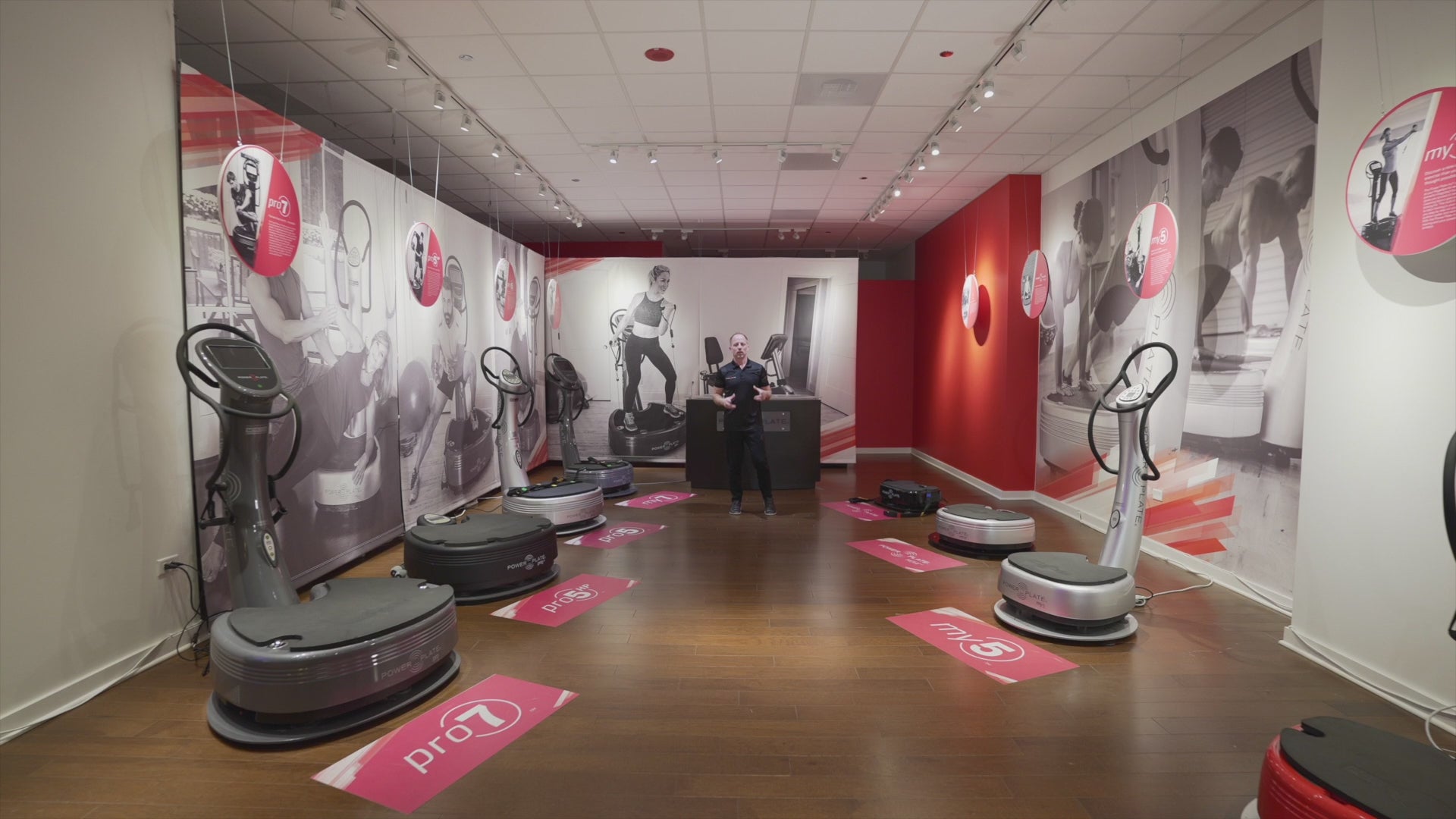 Showroom display featuring multiple Power Plate vibration plate models, including Pro7HC, Pro7, Pro5, My7, My5 and MOVE, arranged on a wooden floor with branded wall graphics