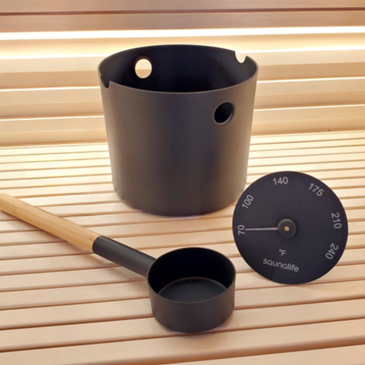 SaunaLife Accessory Package featuring a black sauna bucket, wooden-handled ladle, and thermometer placed in a sauna