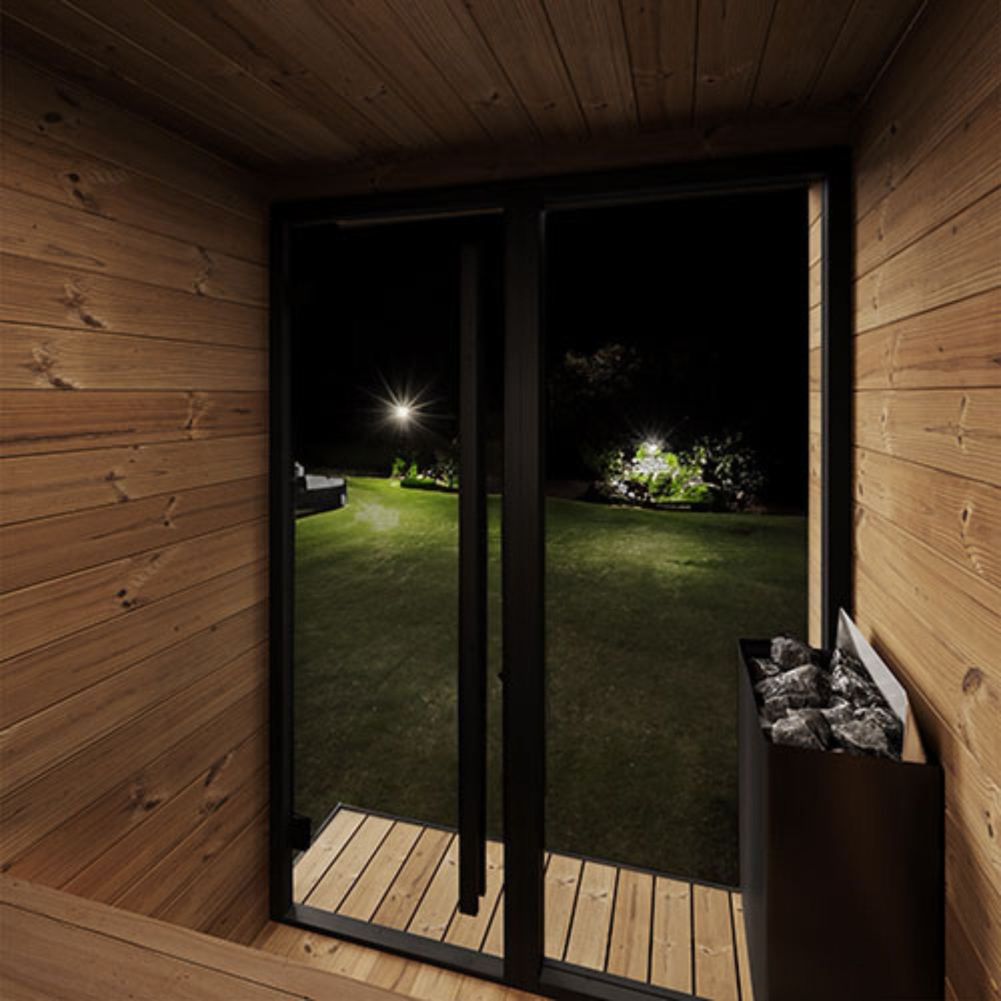 SaunaLife GL4 interior with wood paneling and glass door overlooking the yard at night.