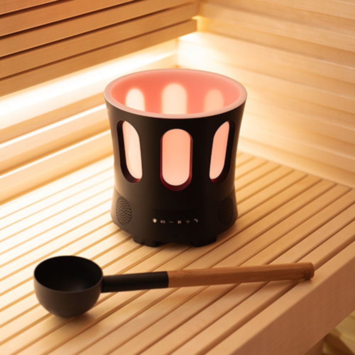 SaunaLife SaunaZone LED speaker bowl glowing with warm light on a wooden sauna bench, paired with a ladle.