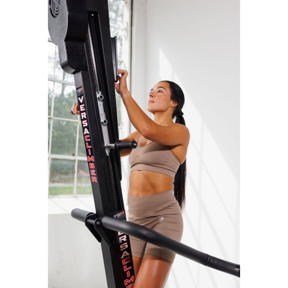 Woman exercising on the VersaClimber TS-M Magnetic in regular black, demonstrating full-body zero-impact cardio and strength training in a modern studio setting.